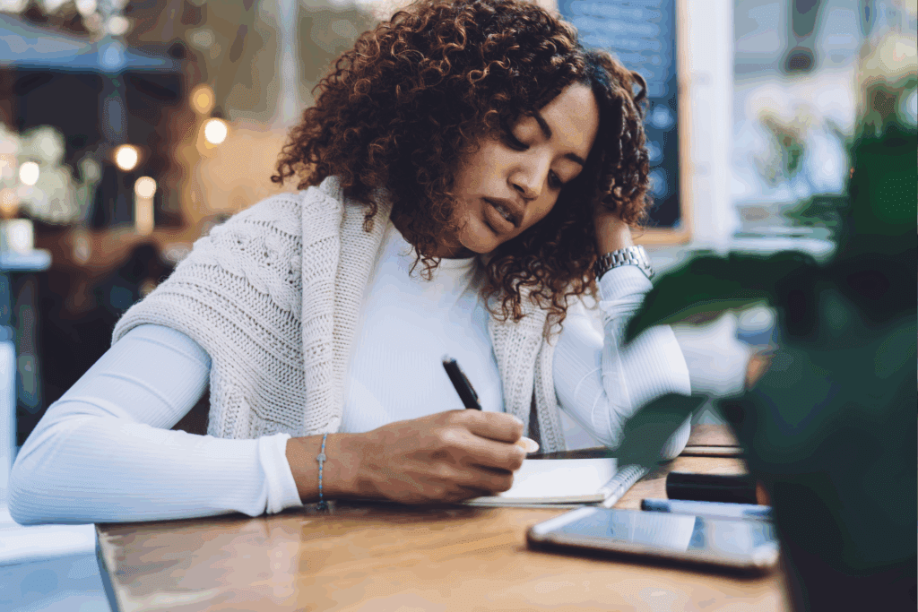 Woman at coffee shop writing small wins after failure in journal