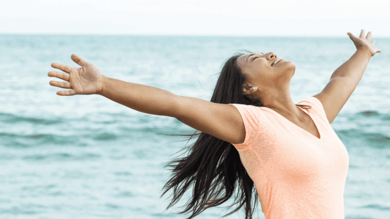 Woman over 35 standing at sunrise with arms open, symbolizing create a meaningful and aligned life”