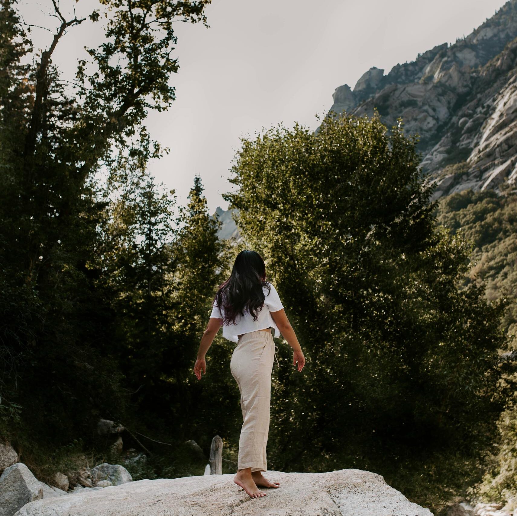 A woman standing on a boulder in the mountainous landscape of Utah, surrounded by trees.