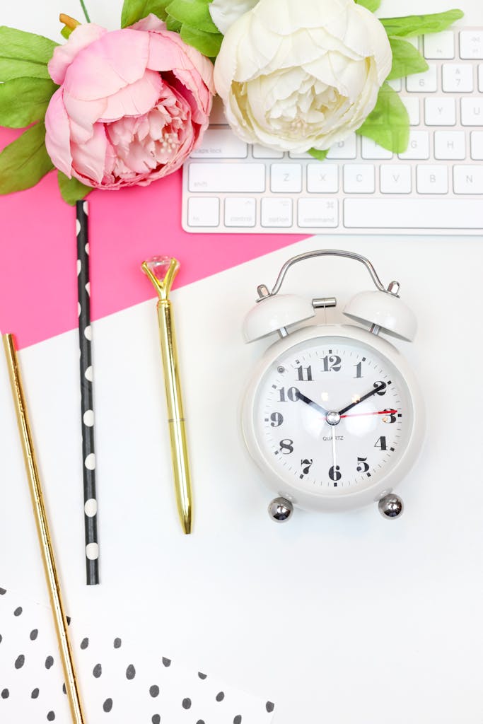 Colorful flat lay featuring an alarm clock, flowers, and stationery items on a desk.