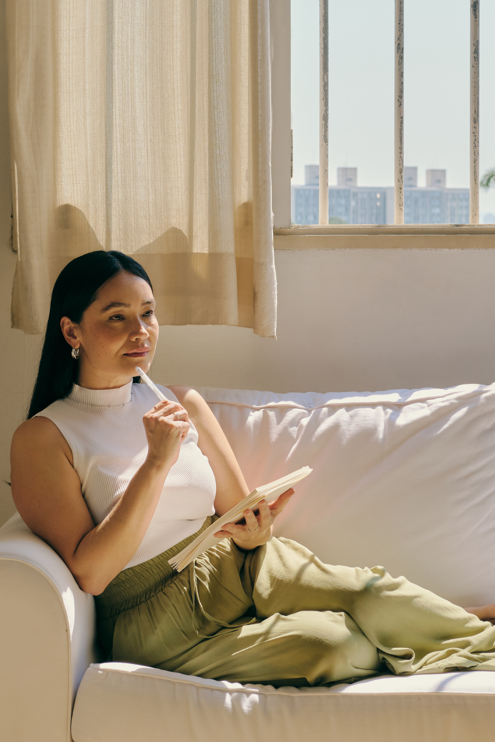 A woman in her late 30s to 50s journaling by a window, soft morning light.
