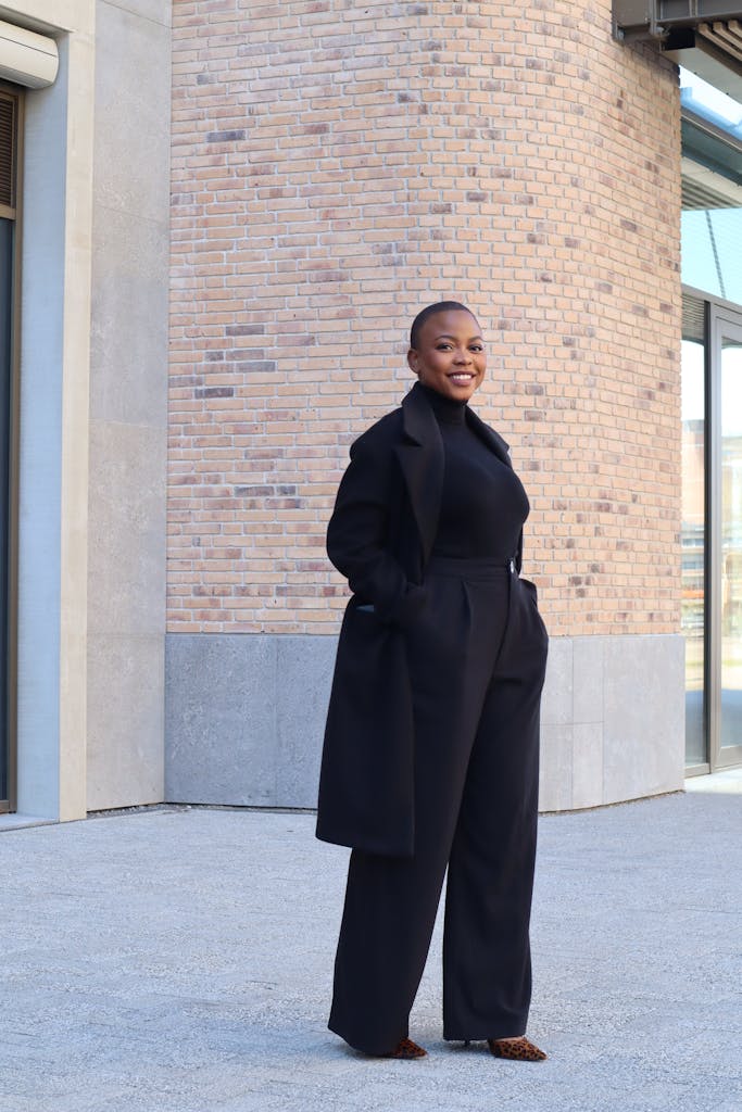Elegant woman in black attire smiling and posing against urban backdrop outdoors in Amsterdam.
