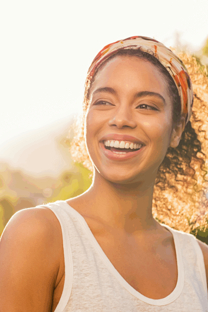Confident woman smiling slightly, outdoors or in a sunlit room signifies, shes stop feeling behind in life.