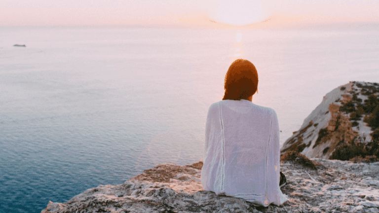 A woman standing at a sunrise or cliff, looking forward with determination.