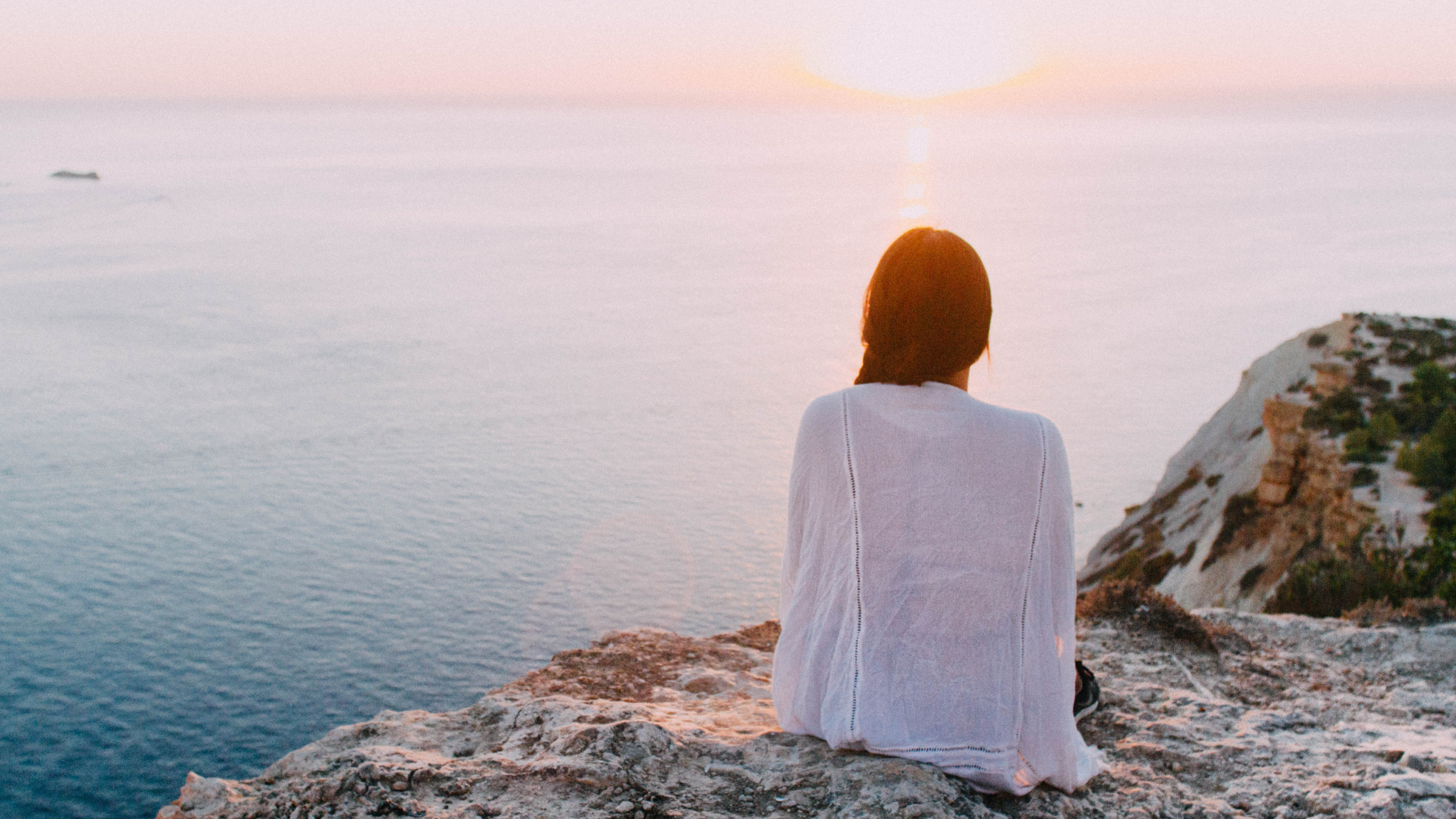 A woman standing at a sunrise or cliff, looking forward with determination.