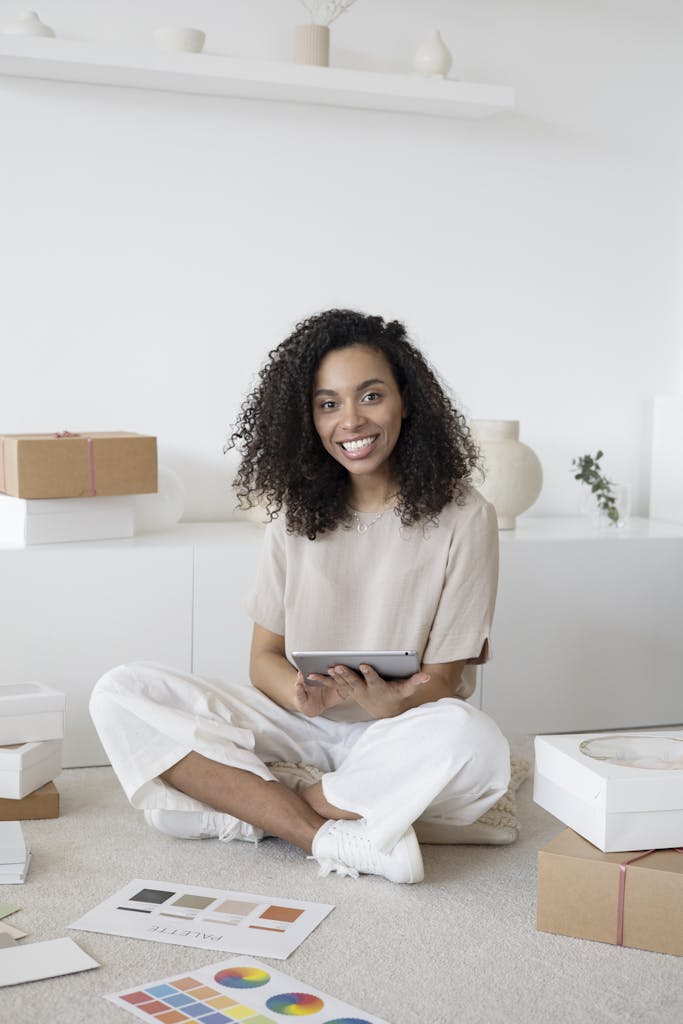A confident young woman sitting among packages and papers while using a tablet, showcasing modern entrepreneurship.