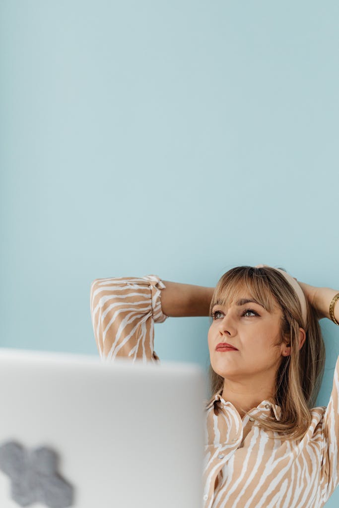 Contemplative woman in striped blouse seated at desk, pondering with hands behind head. Afraid of Failing at Starting Over
